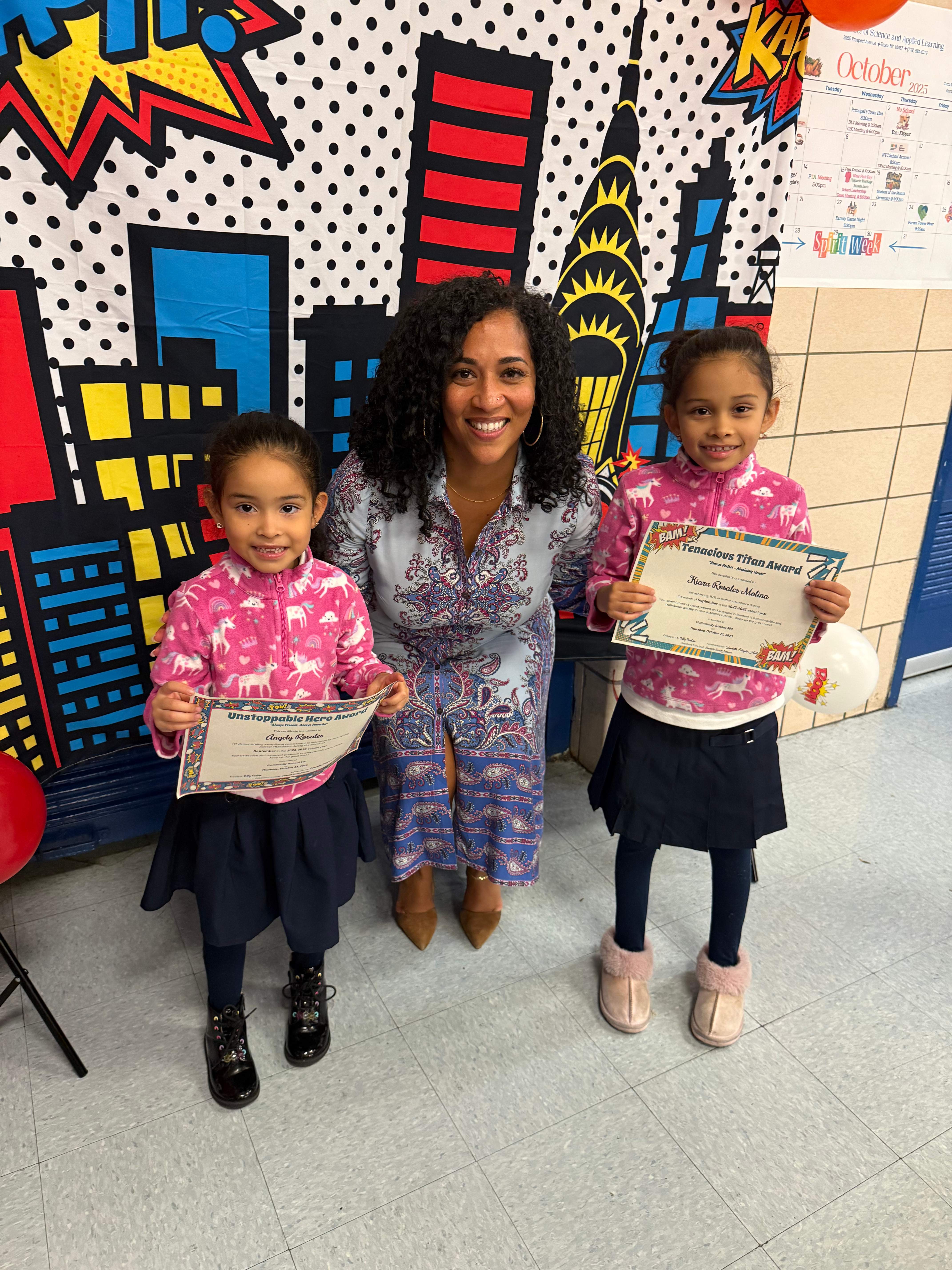 Two students holding award certificates with smiling adult in school hallway