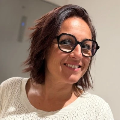 Photo d'Elisabeth Bennecib avec une coupe au carré, des lunettes de vue noires et un haut blanc