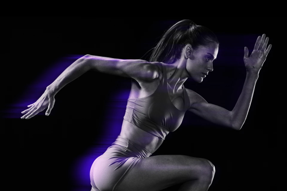 Athletic woman mid-sprint with purple lighting on a dark background