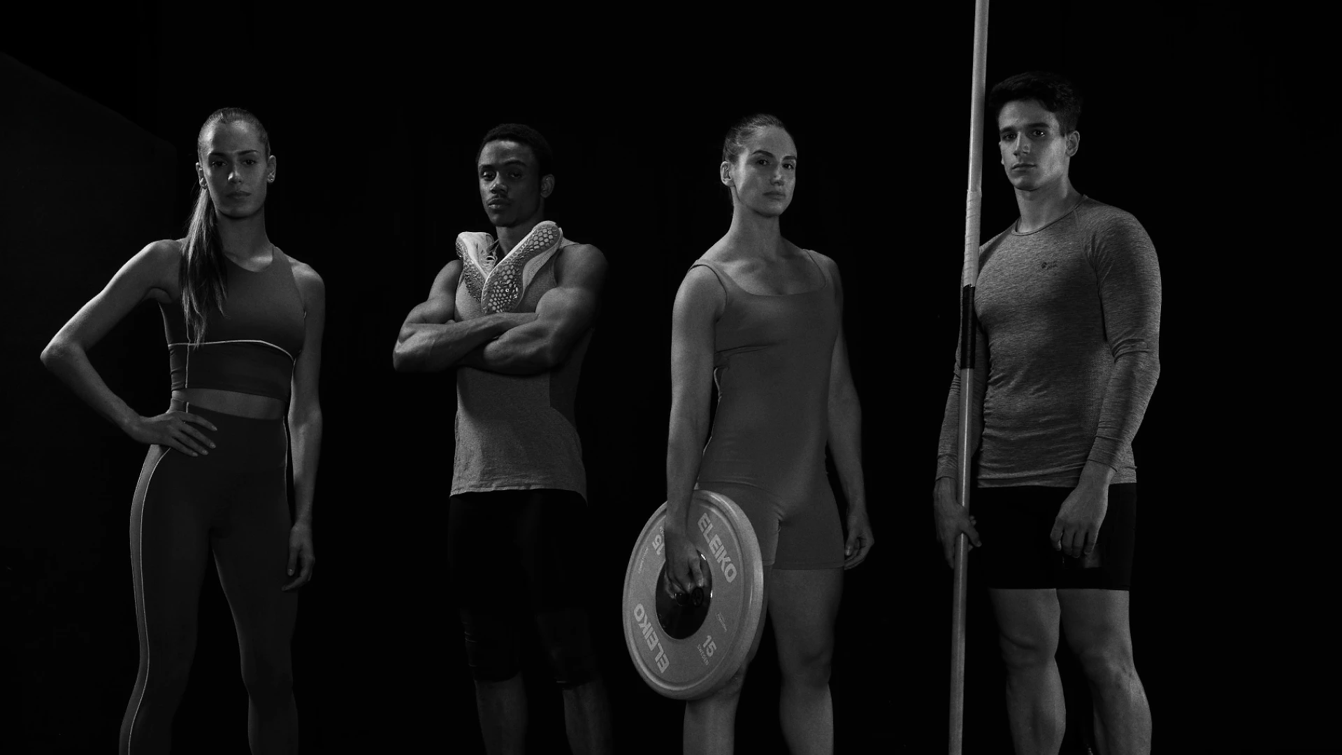 Four athletes in athletic wear posing in a dramatic black-and-white studio portrait