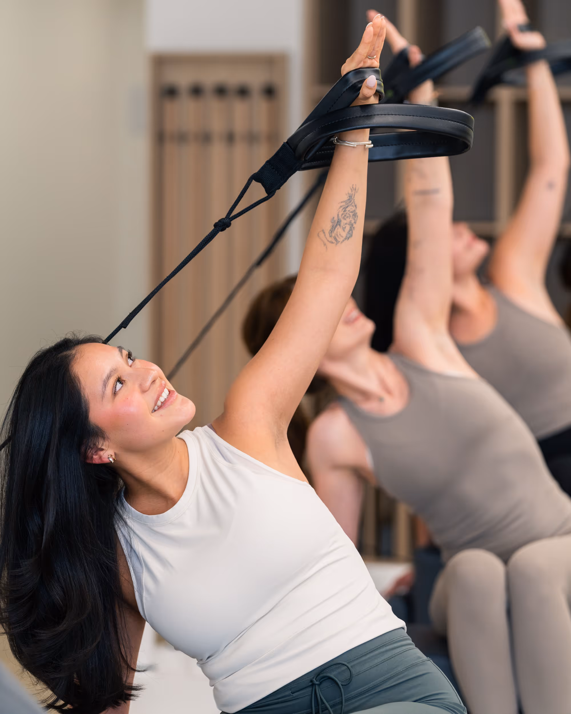 Three women stretching arms upward using Pilates rings in a fitness studio.