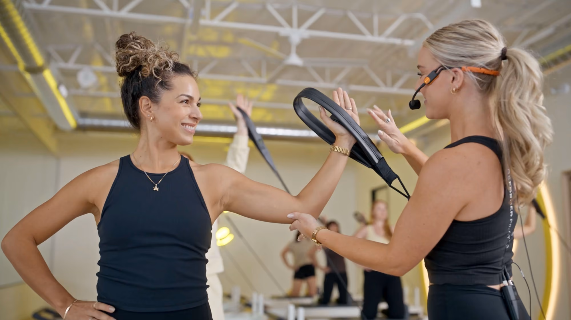 Fitness instructor holding a resistance band as a woman stretches her arm during a workout class.
