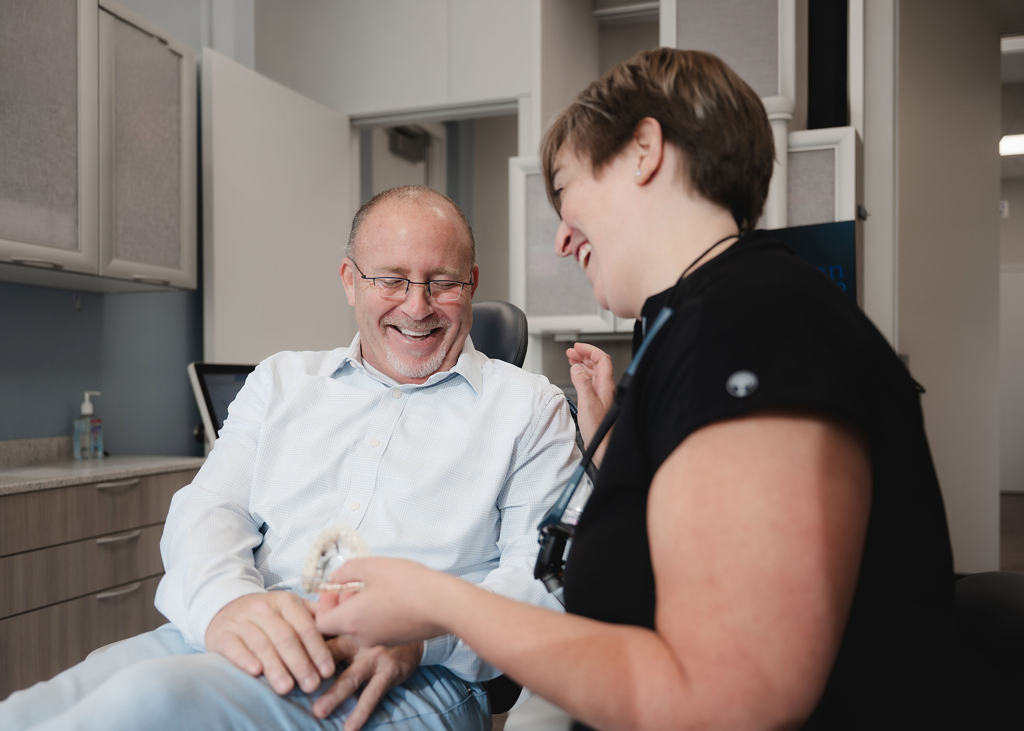 A smiling male patient in a dental chair interacting with a female dentist holding a dental mold.