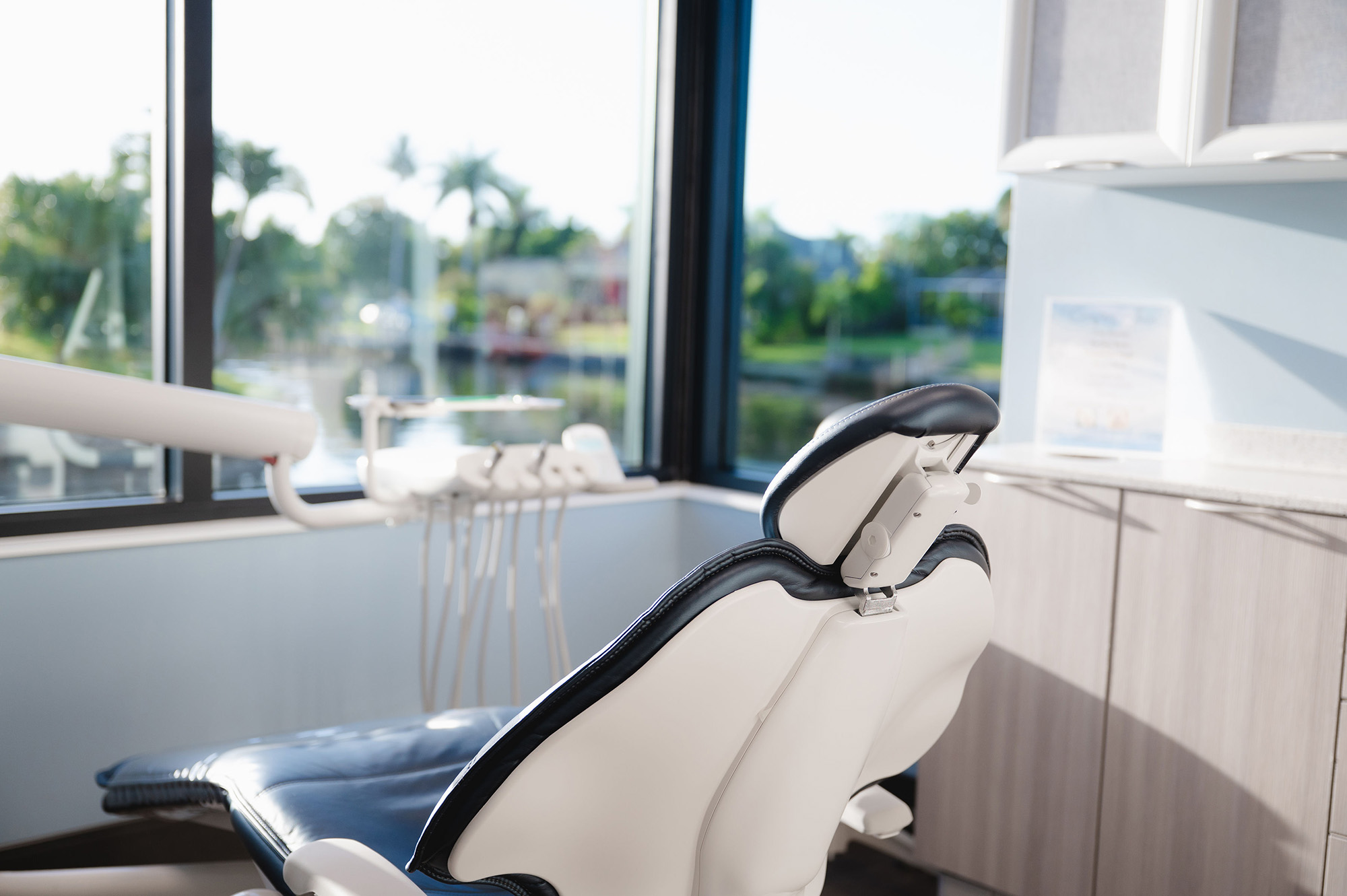 Modern dental chair in a bright clinic room with large windows showing greenery outside.
