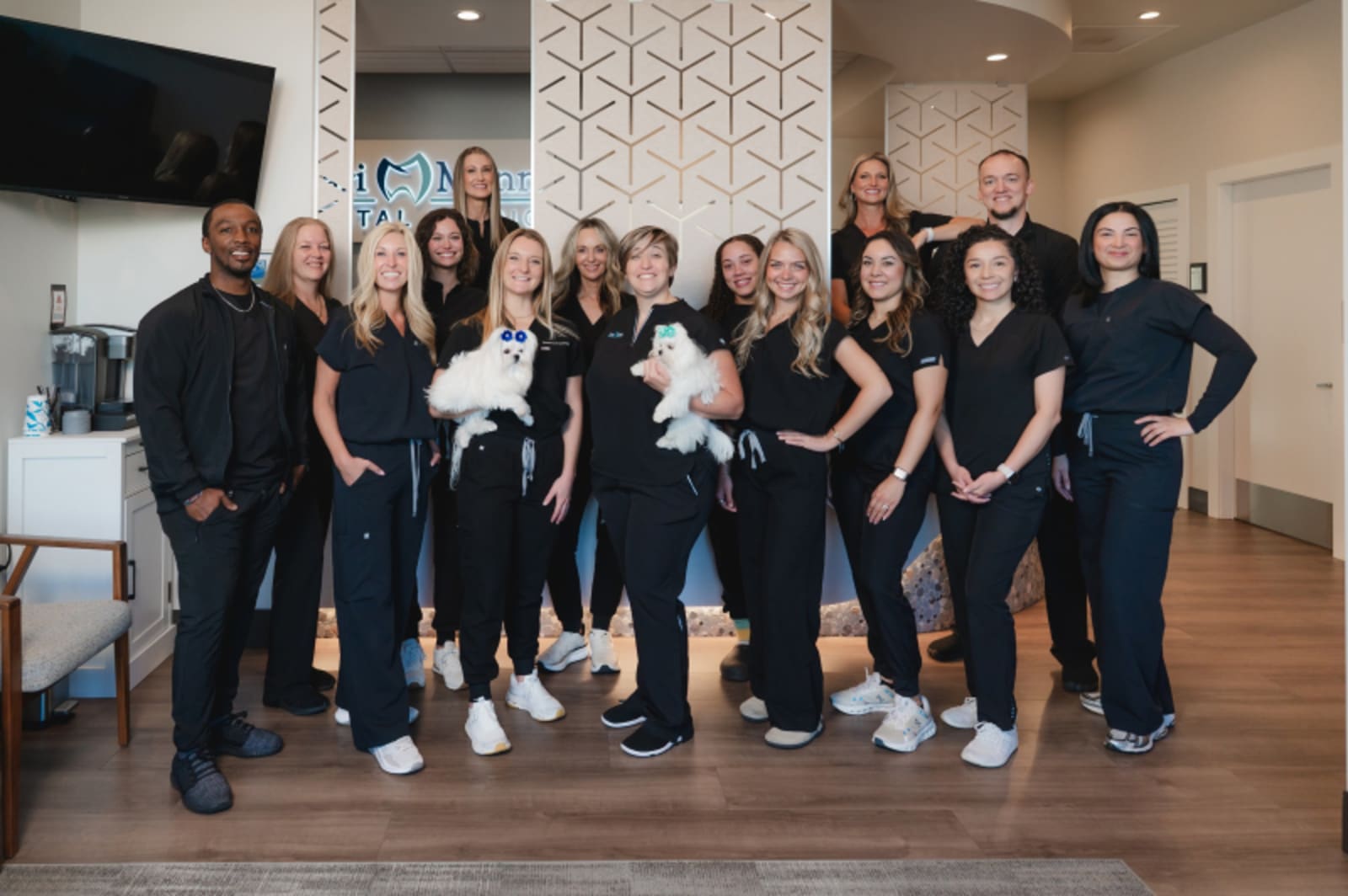 Kari Mann Dental Studio team posing together in modern office setting wearing black scrubs and white sneakers.
