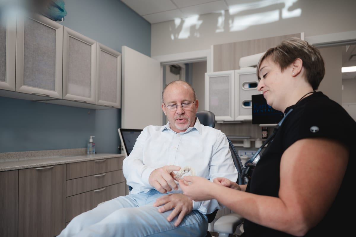 Dentist showing dental implant model to patient in treatment chair during consultation