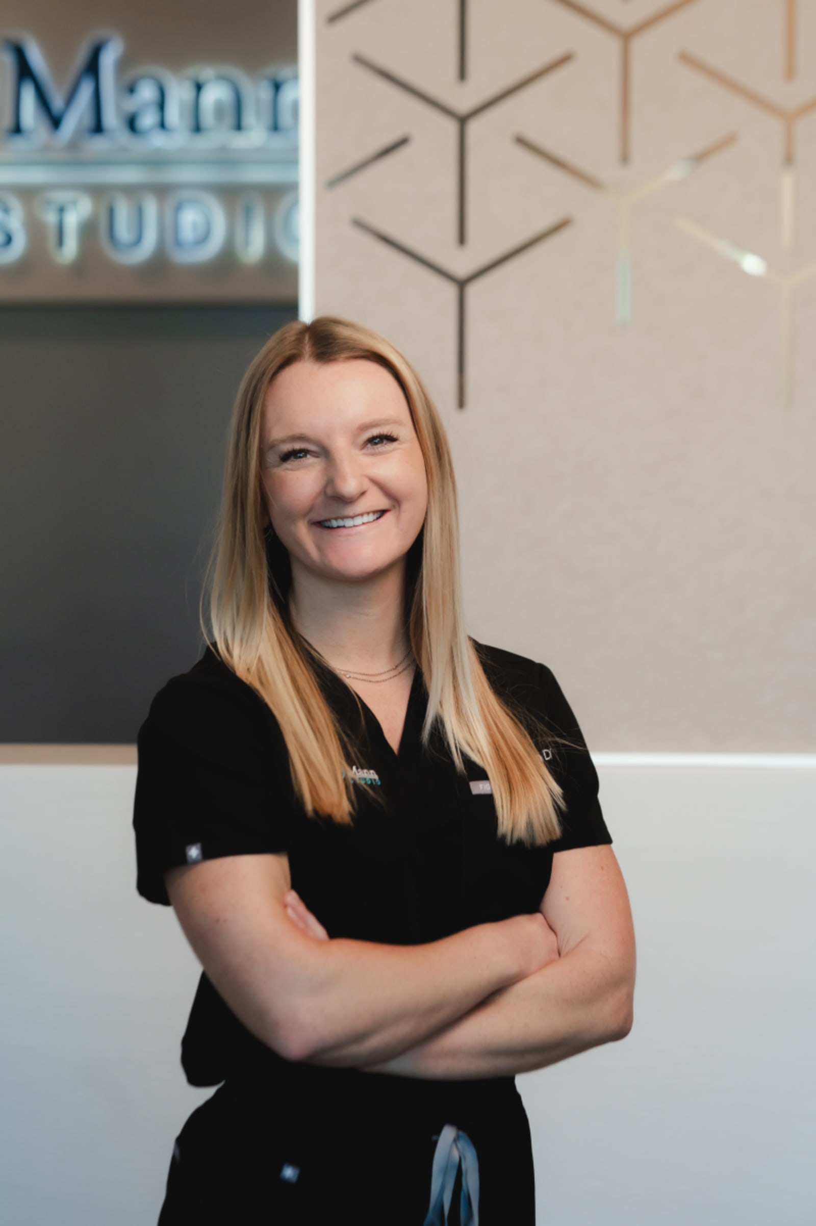 Female dental professional smiling with arms crossed in front of studio signage