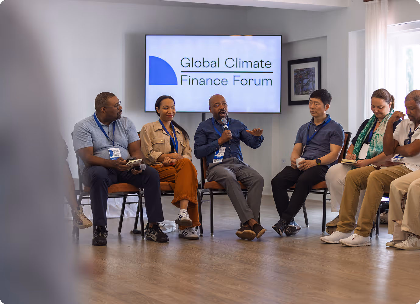 A group of six people sitting in chairs in a panel discussion at the Global Climate Finance Forum, with one man speaking into a microphone.