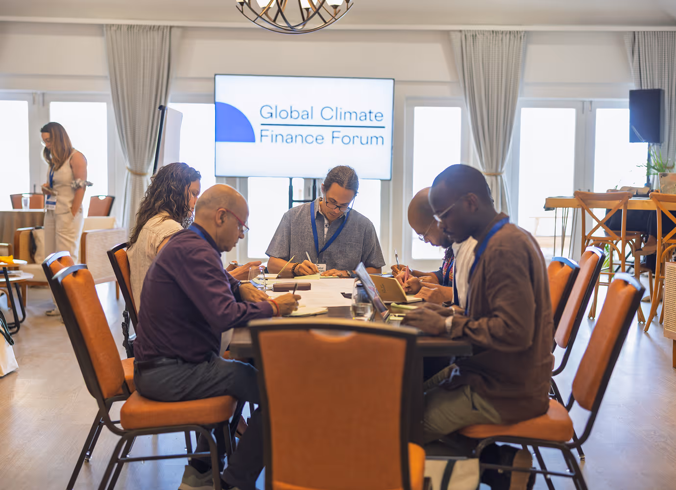 Diverse group of people sitting in a panel discussion, one person speaking into a microphone during a Global Climate Finance Forum event.