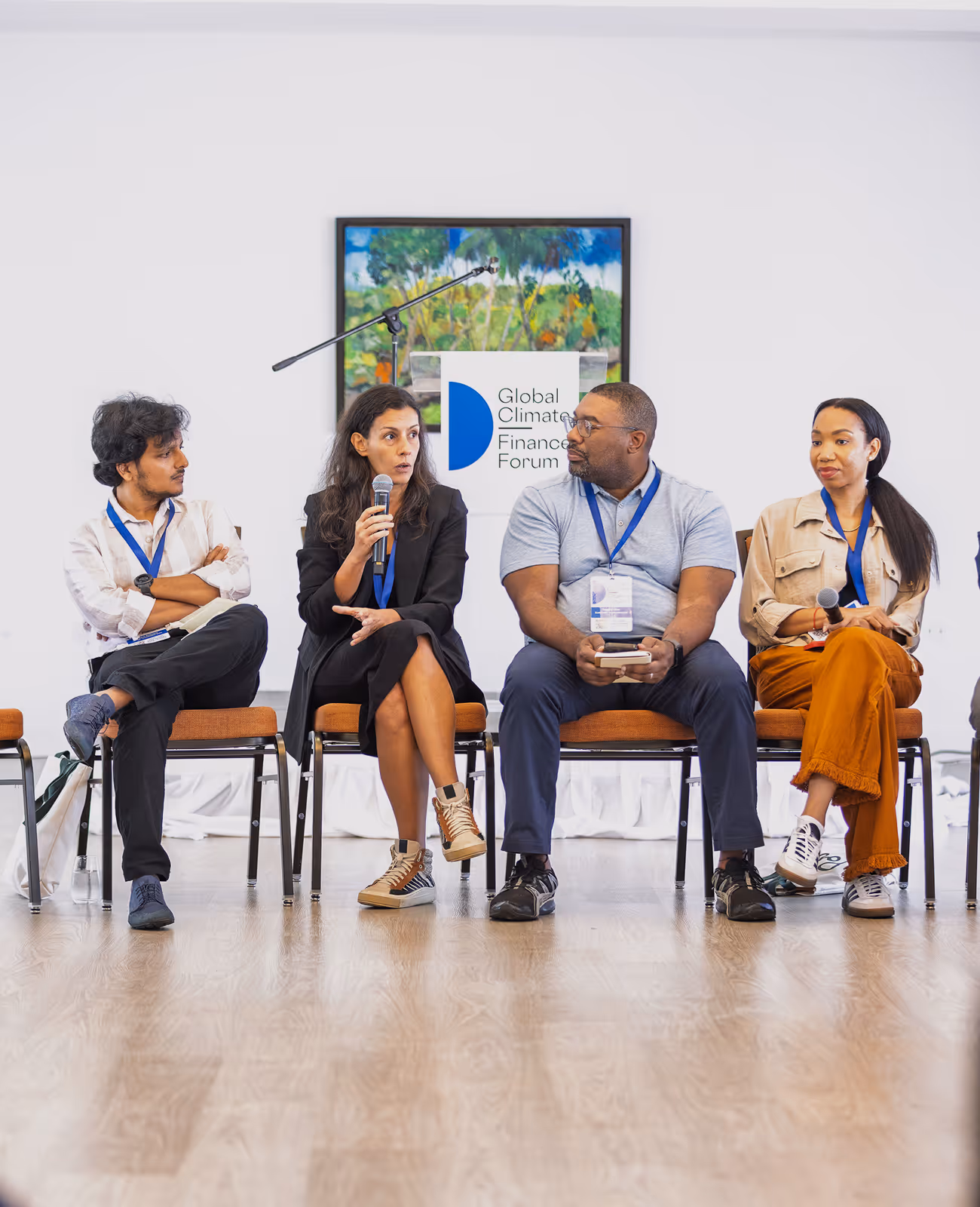 A diverse group of five people sitting in chairs in a panel discussion, with one woman speaking into a microphone.