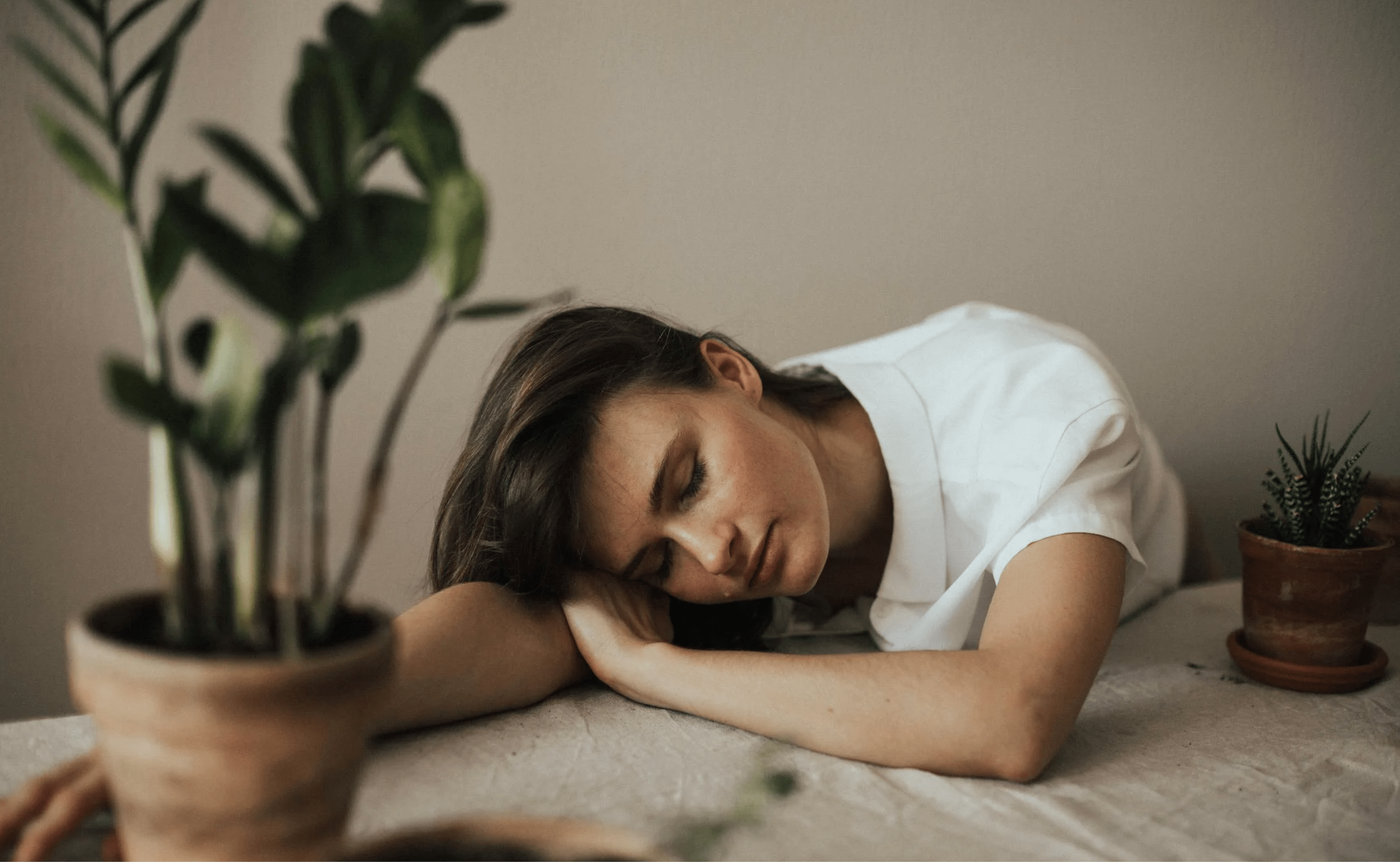  A woman in a white shirt resting her head on a table, appearing to nap.