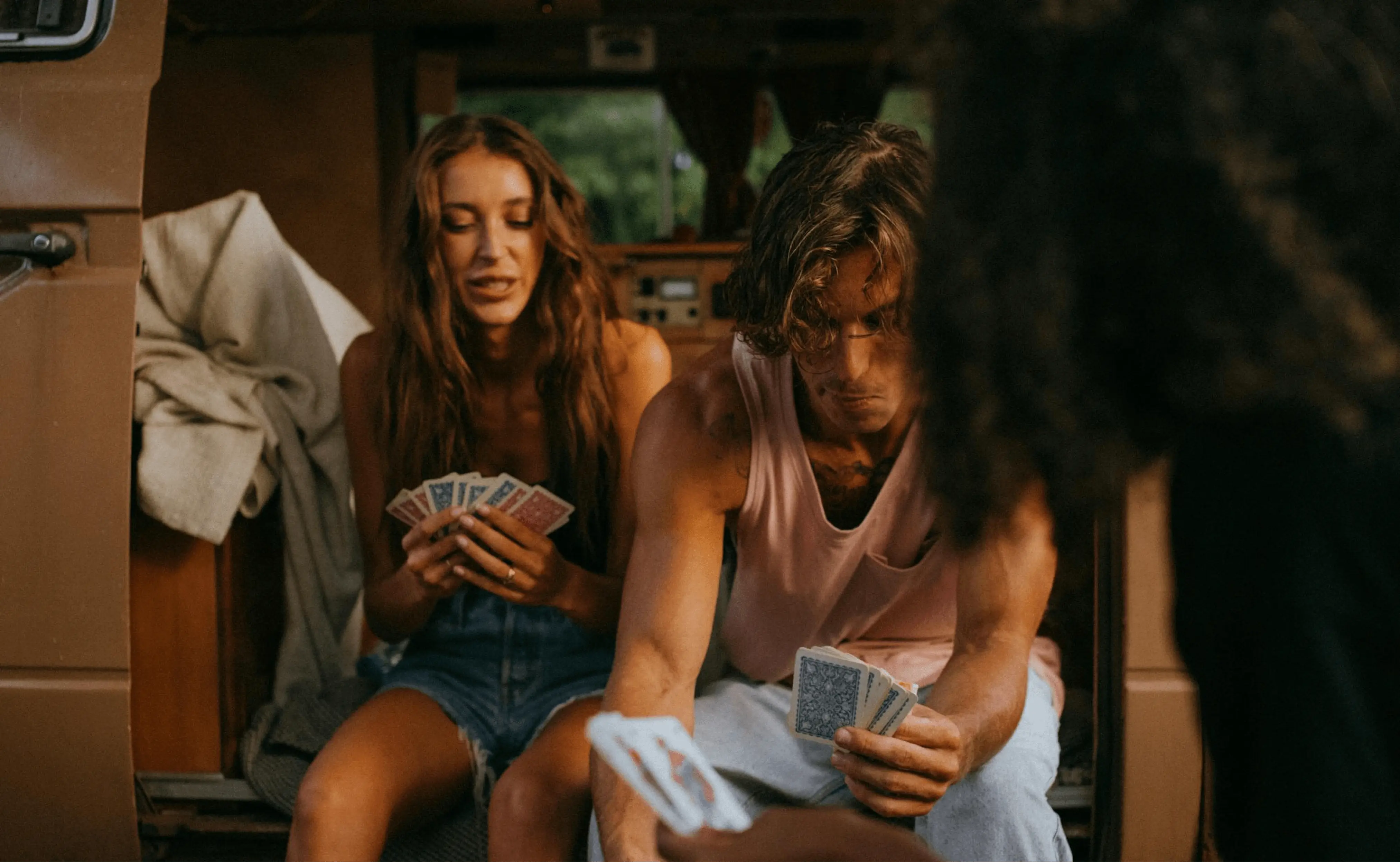 A group of friends is sitting inside a van playing cards. The atmosphere appears casual and relaxed, with the friends deeply engaged in the game.
