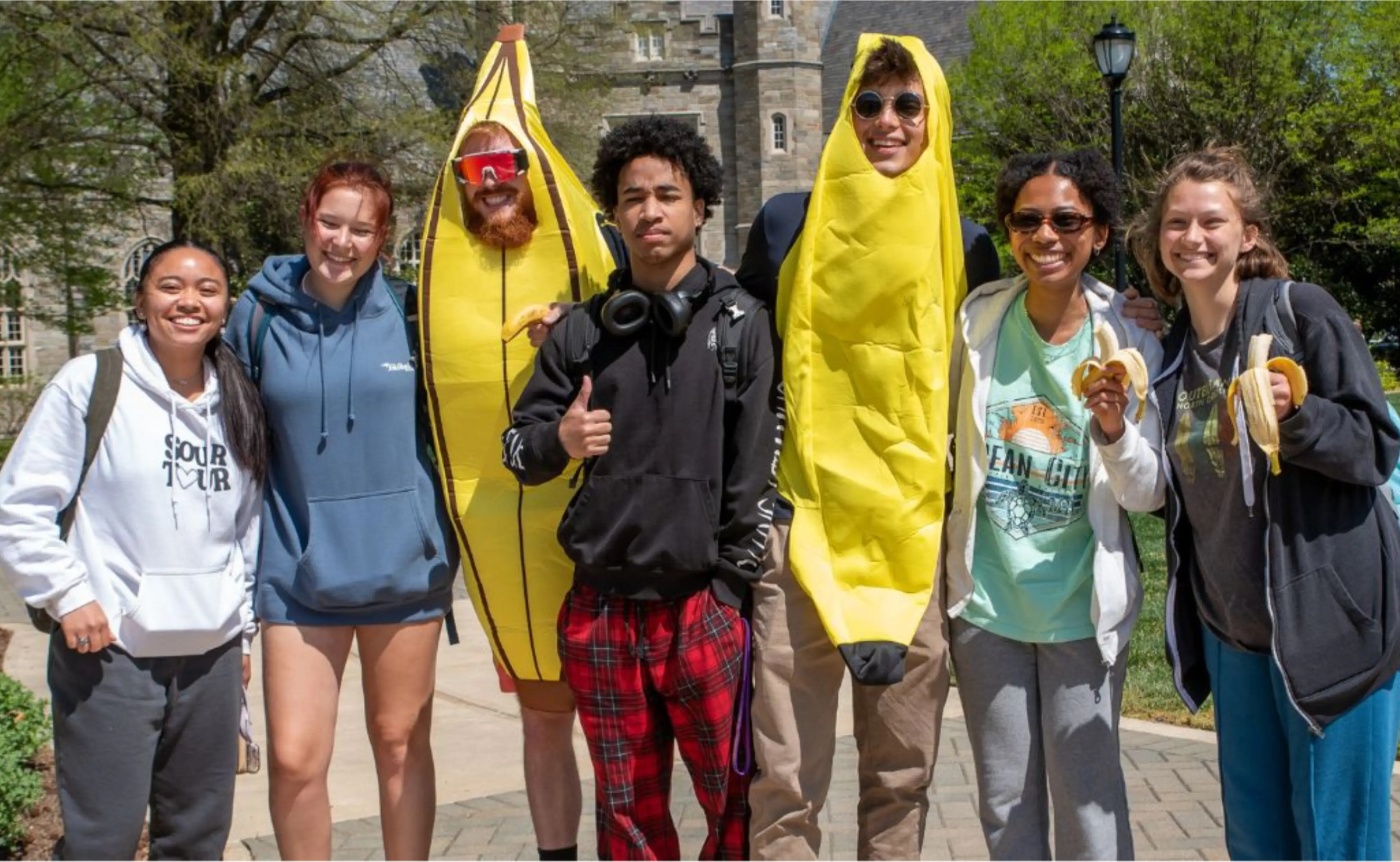 A group of university students smiling at the camera. Two are wearing banana costumes.
