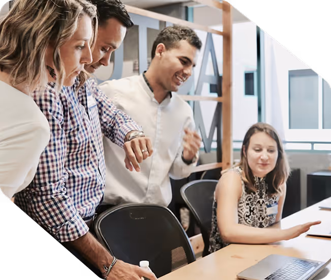 Four professionals engaged in a discussion around a conference table with a laptop in an office setting.