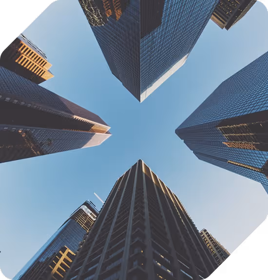 View looking up at five tall skyscrapers surrounding a clear blue sky.
