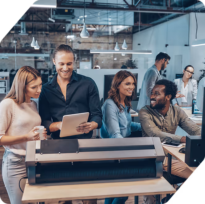 Group of coworkers smiling and collaborating around a cutting machine in a modern office.