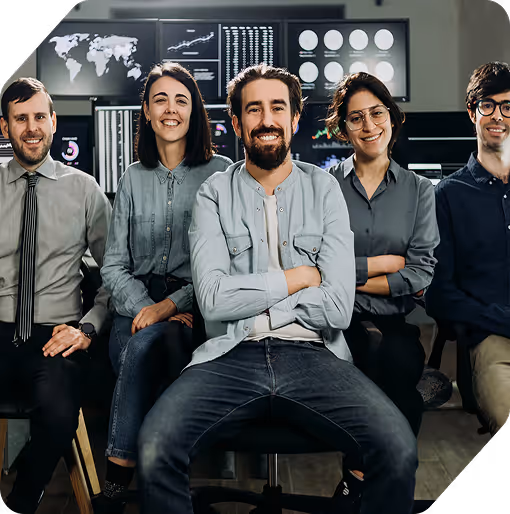 Five young professionals sitting and smiling in front of multiple computer monitors displaying data and maps.