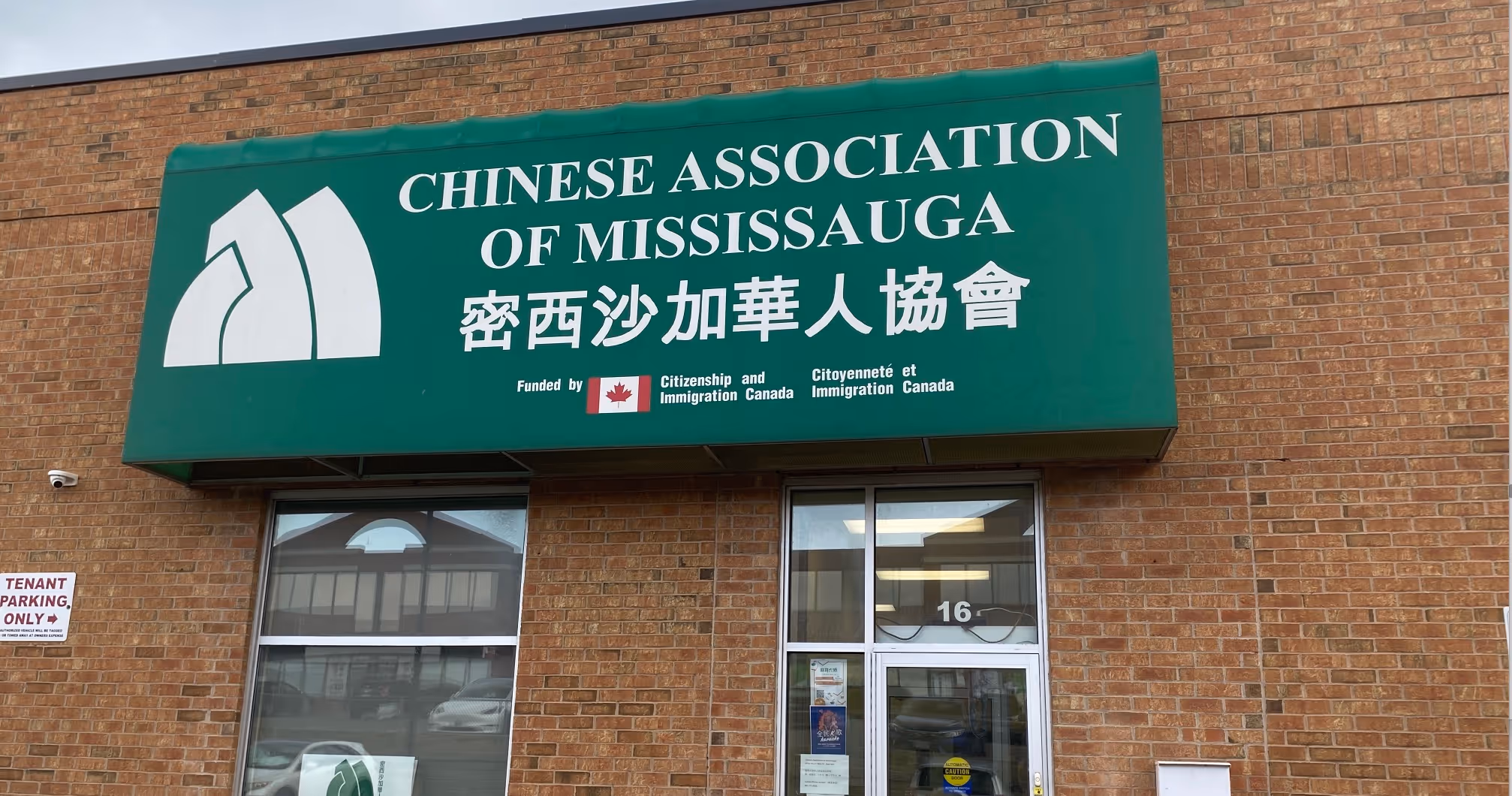Brick building displaying a green sign for the Chinese Association of Mississauga. The entrance has double glass doors, creating a welcoming tone.