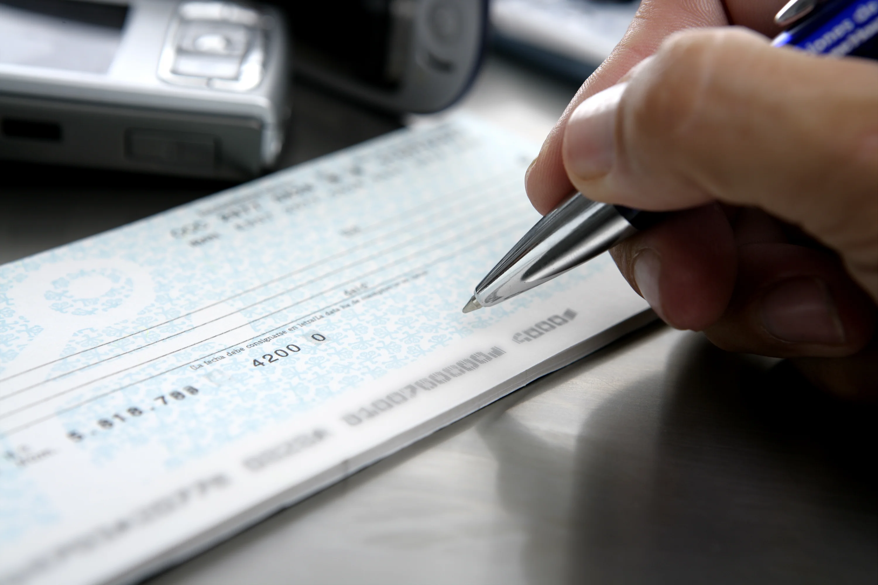 A hand holding a pen writes on a blue bank cheque for donation.