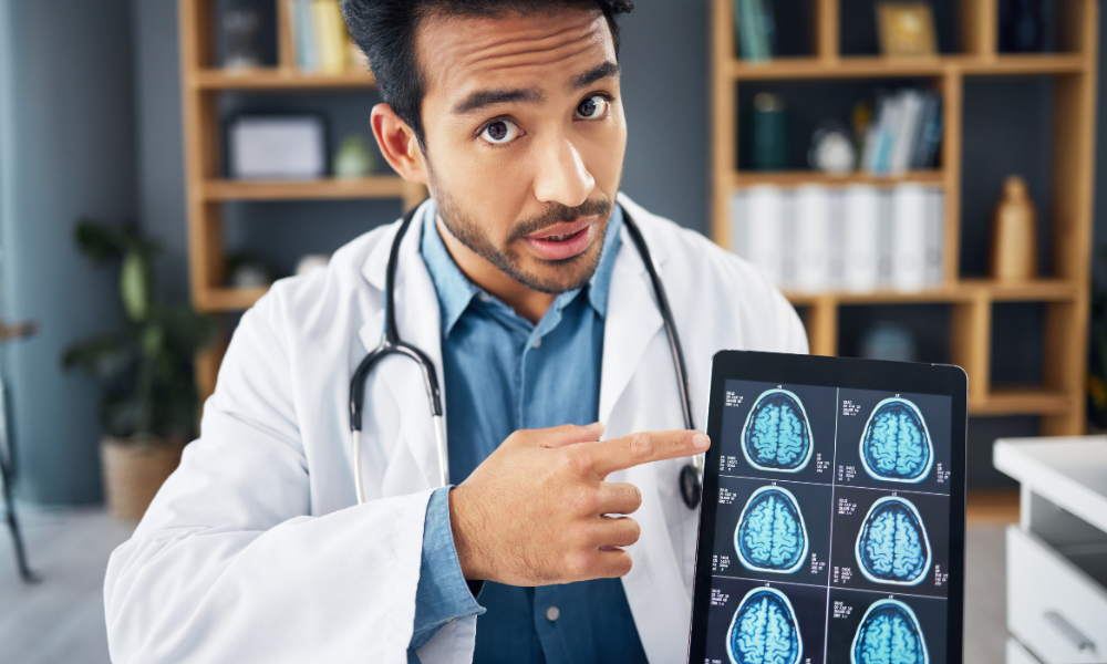 A person holds up a medical scan of multiple brain slices and points to one with their finger.