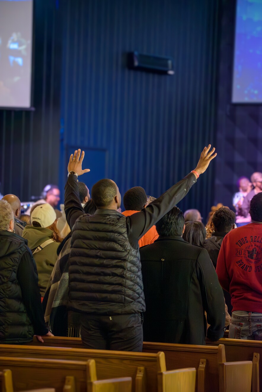 People standing in a church with one man raising both hands in worship or praise.