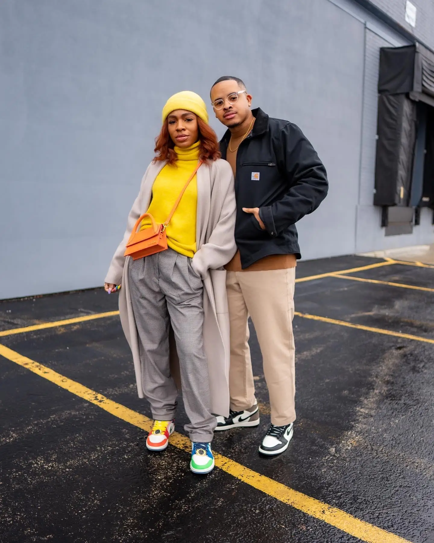 Man and woman standing in a parking lot wearing casual fall outfits and sneakers.