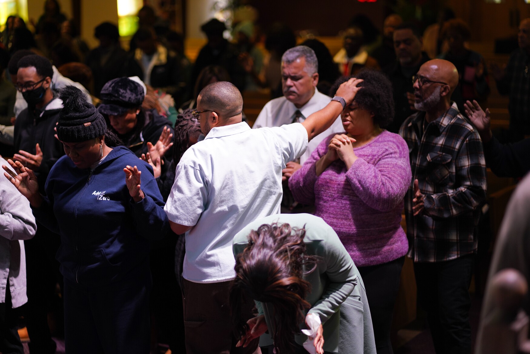 People in prayer during a religious gathering, one man places his hand on a woman's forehead.