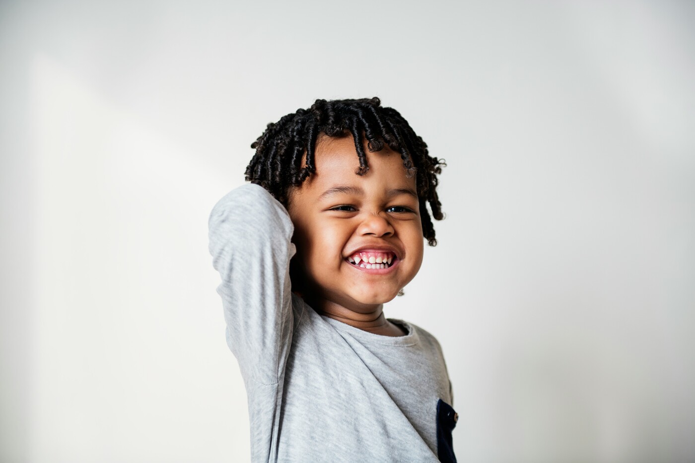 Smiling young child with curly hair wearing a gray shirt against a plain light background.