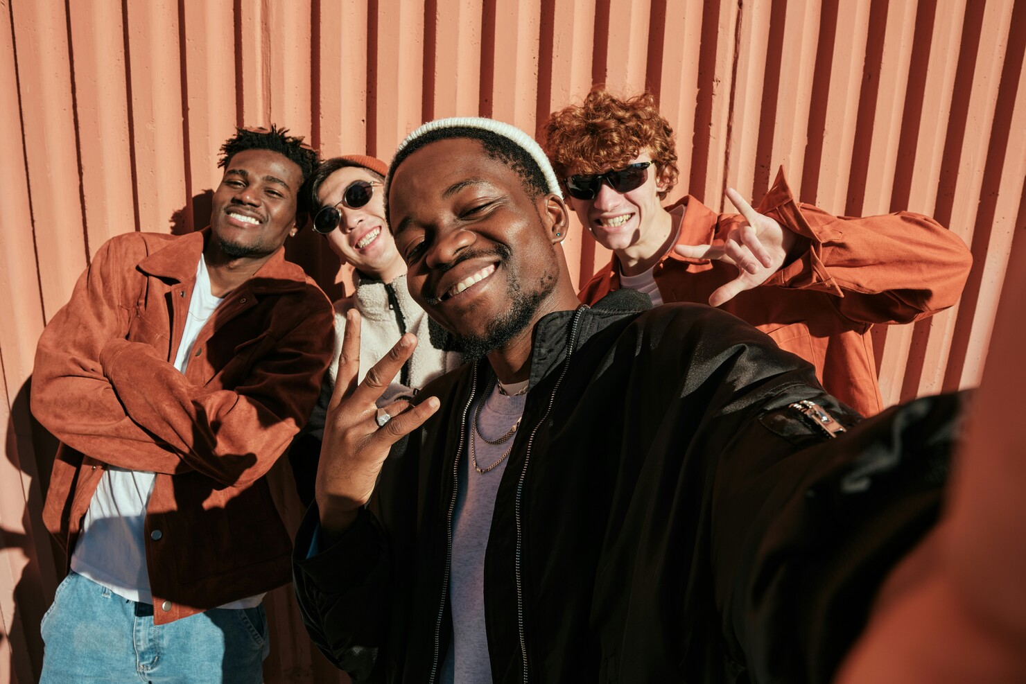 Four young men smiling and posing for a selfie against a textured, orange wall background.