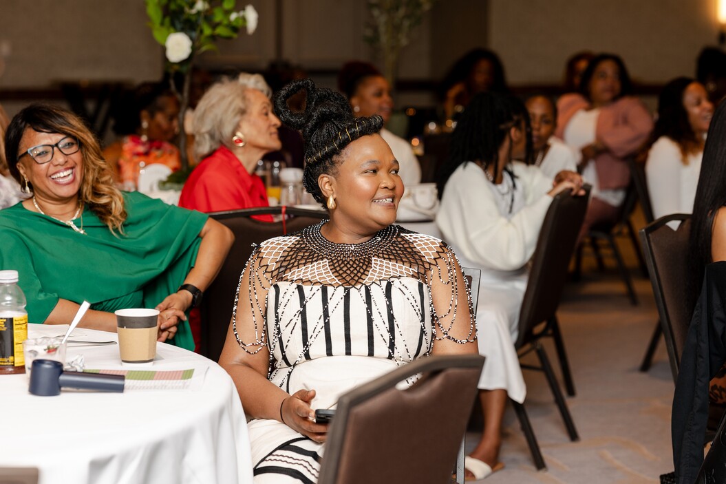 Women sit at tables in a banquet hall, some smiling and engaged in conversation.
