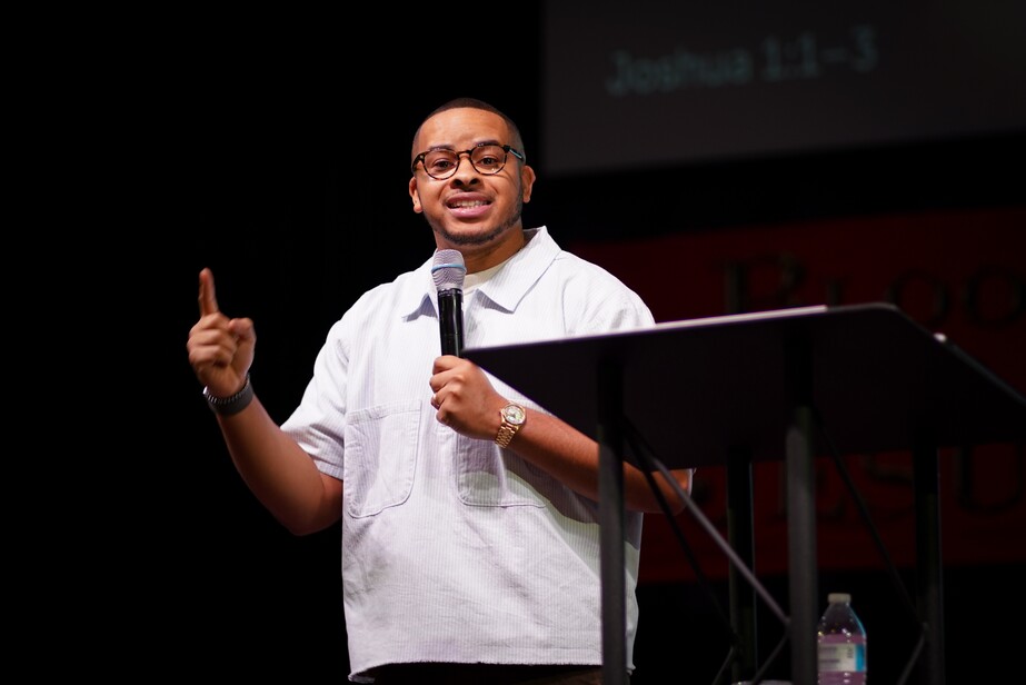 Man wearing glasses speaking into microphone while gesturing during a presentation on stage.