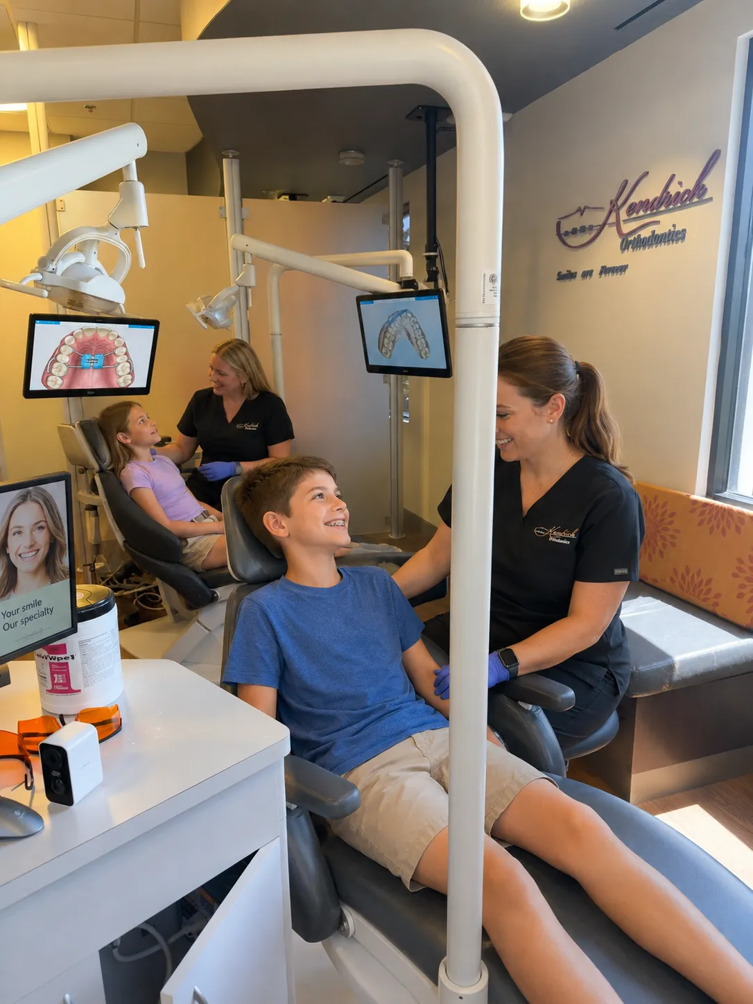 Children in treatment chairs with orthodontic assistants in a bright orthodontic clinic