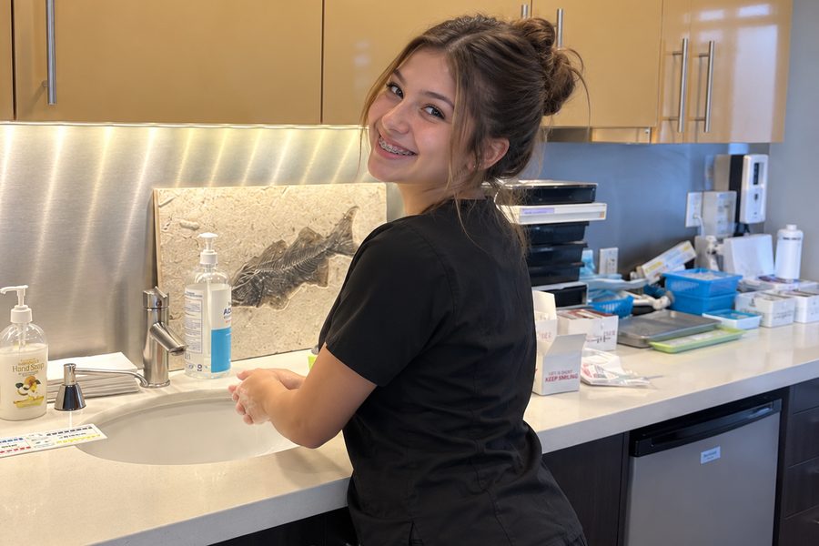 Smiling young woman with braces washing her hands in an orthodontic office