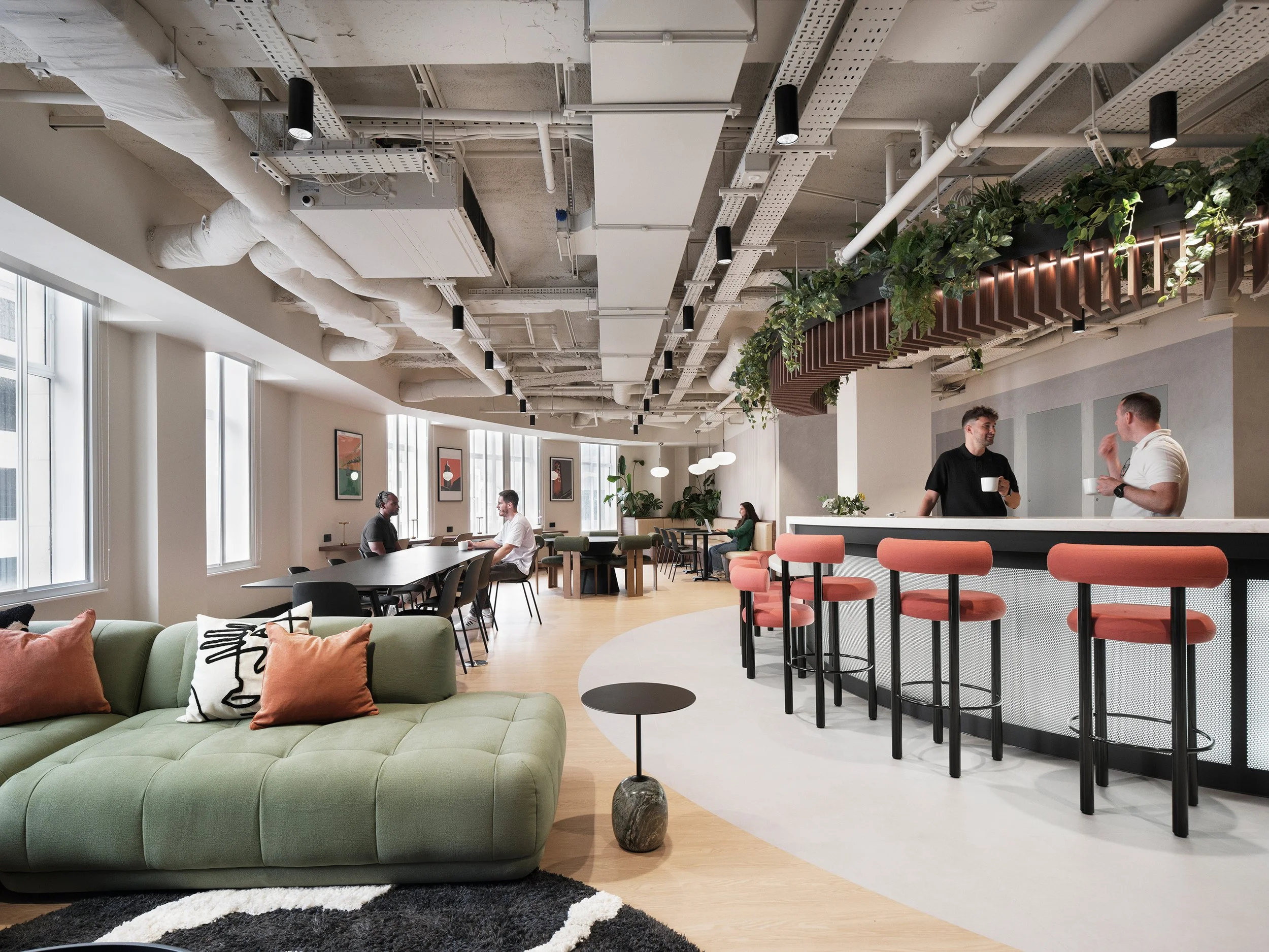Office lounge with a green sofa and orange bar where two colleagues talk, at Banking Circle