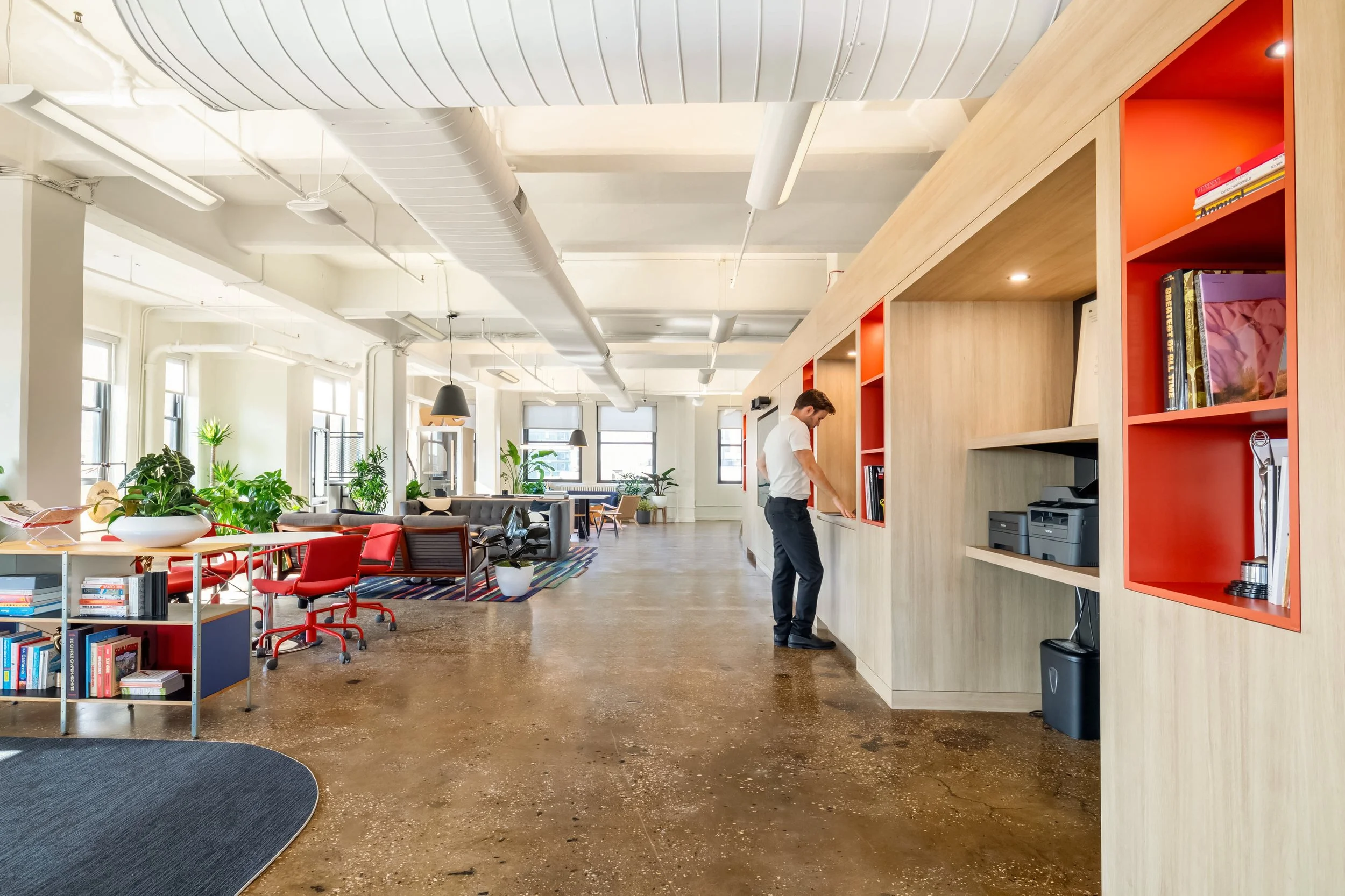 Open-plan loft office with polished concrete floor, orange shelving and a person walking