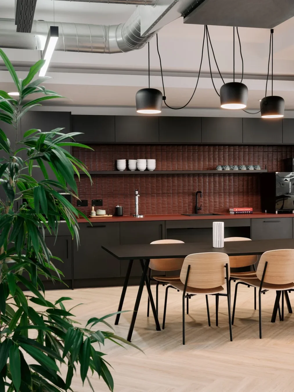 Office kitchen and dining area with dark cabinetry, terracotta tiling and a timber table at Palantir