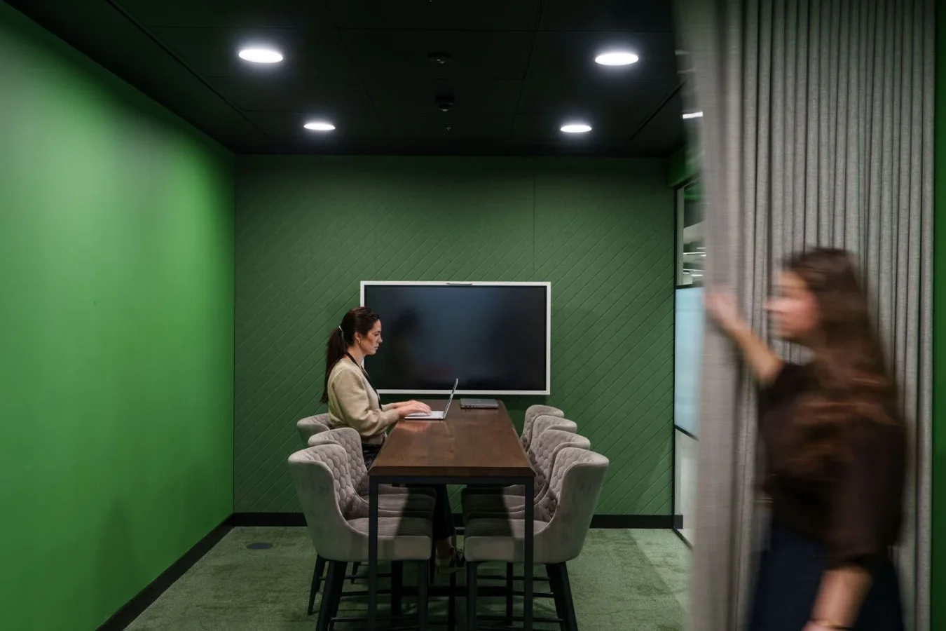 Person walking past a green-walled meeting room with a presentation screen at Schneider Electric