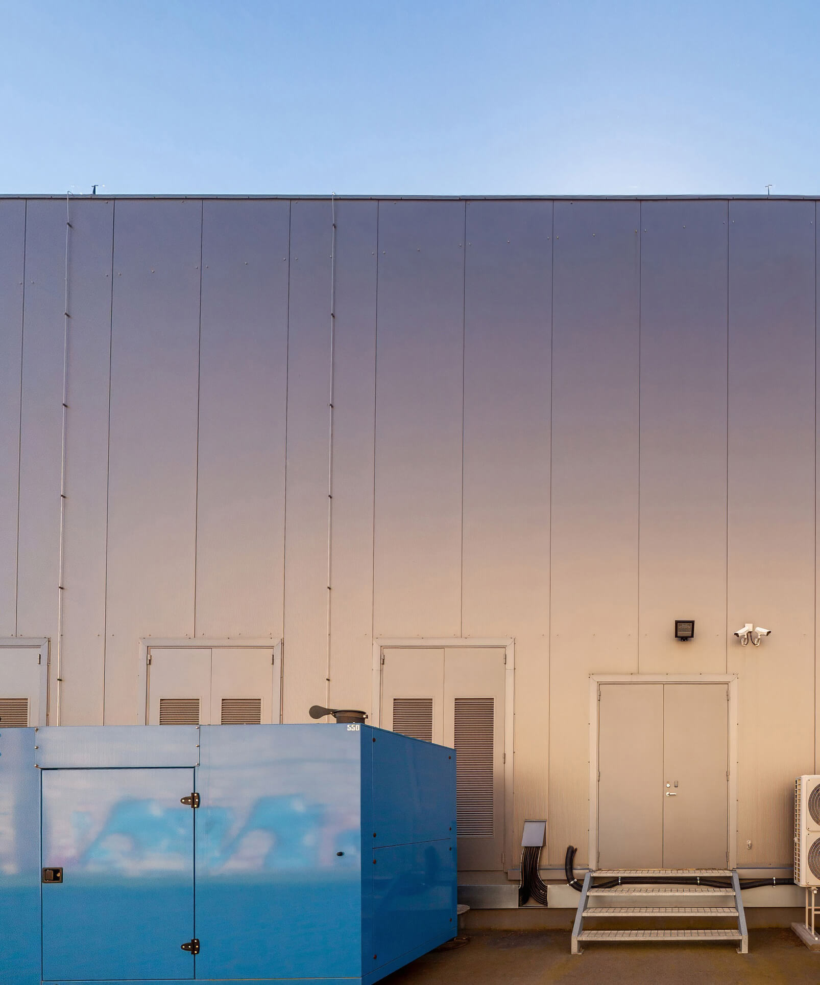 Industrial building exterior at dusk with a blue generator unit in the foreground