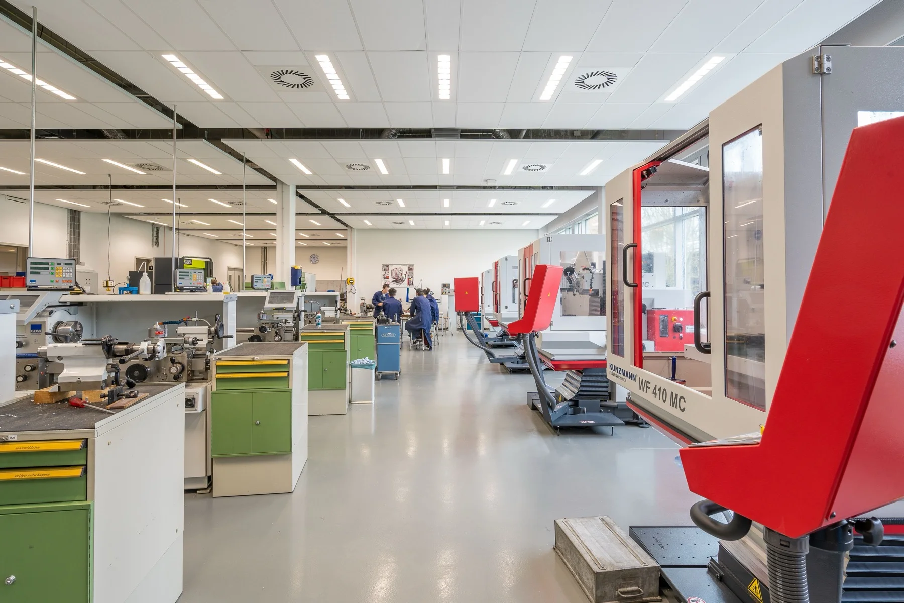 Spacious industrial workshop with machining equipment and people walking the central aisle