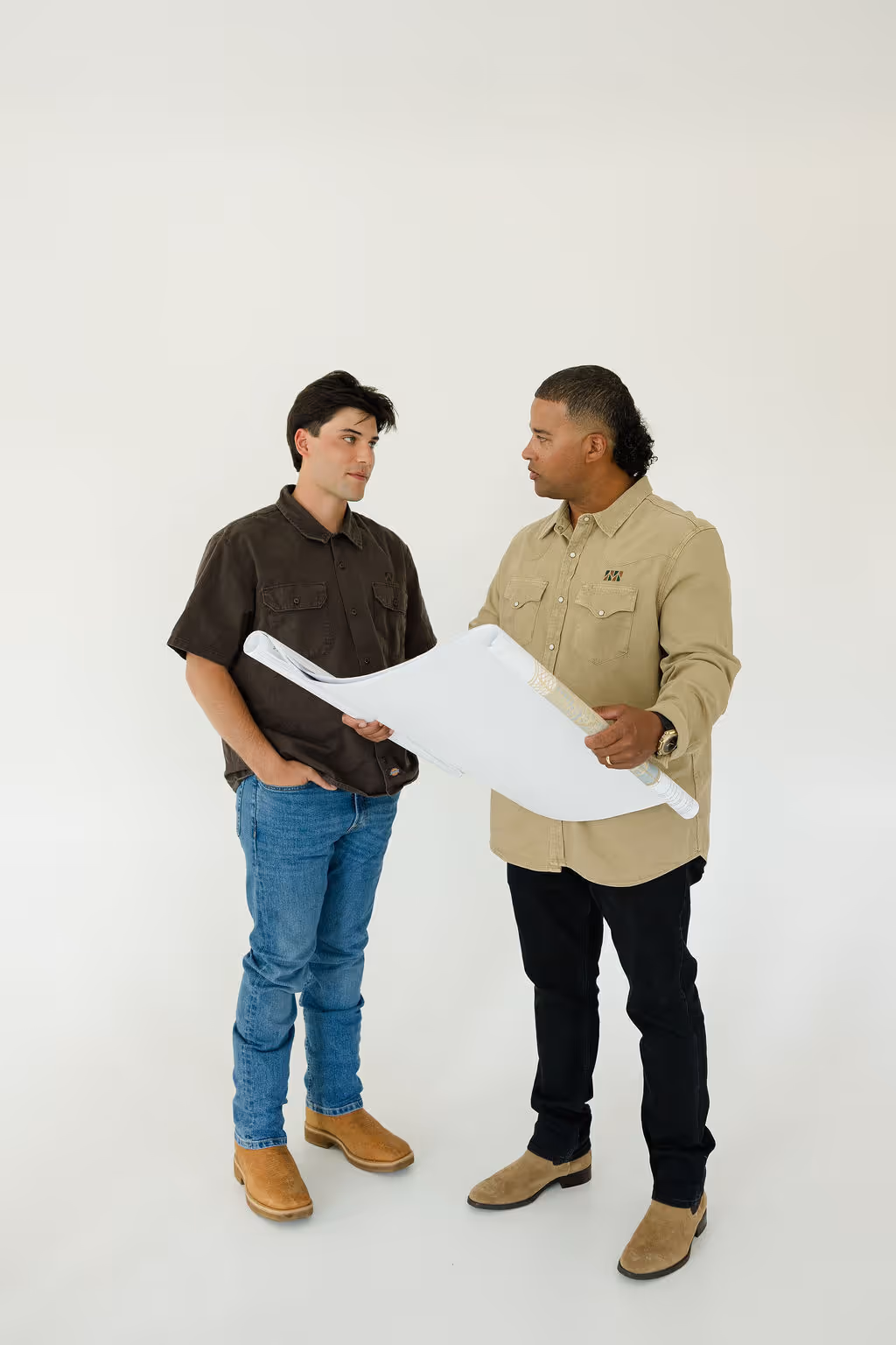Two men discussing a rolled architectural blueprint against a plain white background.