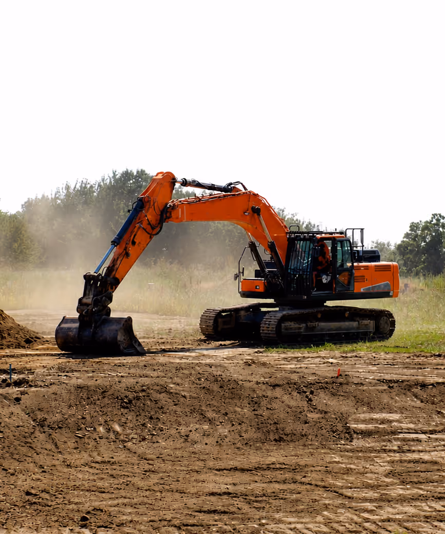 Orange excavator digging dirt at a construction site with trees in the background.