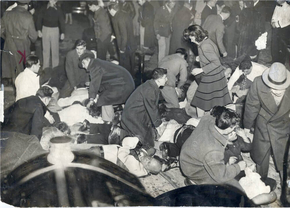 Photo of a crowd of people, some lying down, some standing, outside in the street.
