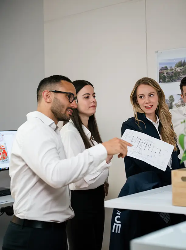 Drei Personen in formeller Kleidung diskutieren und betrachten einen Plan in einem Büro.