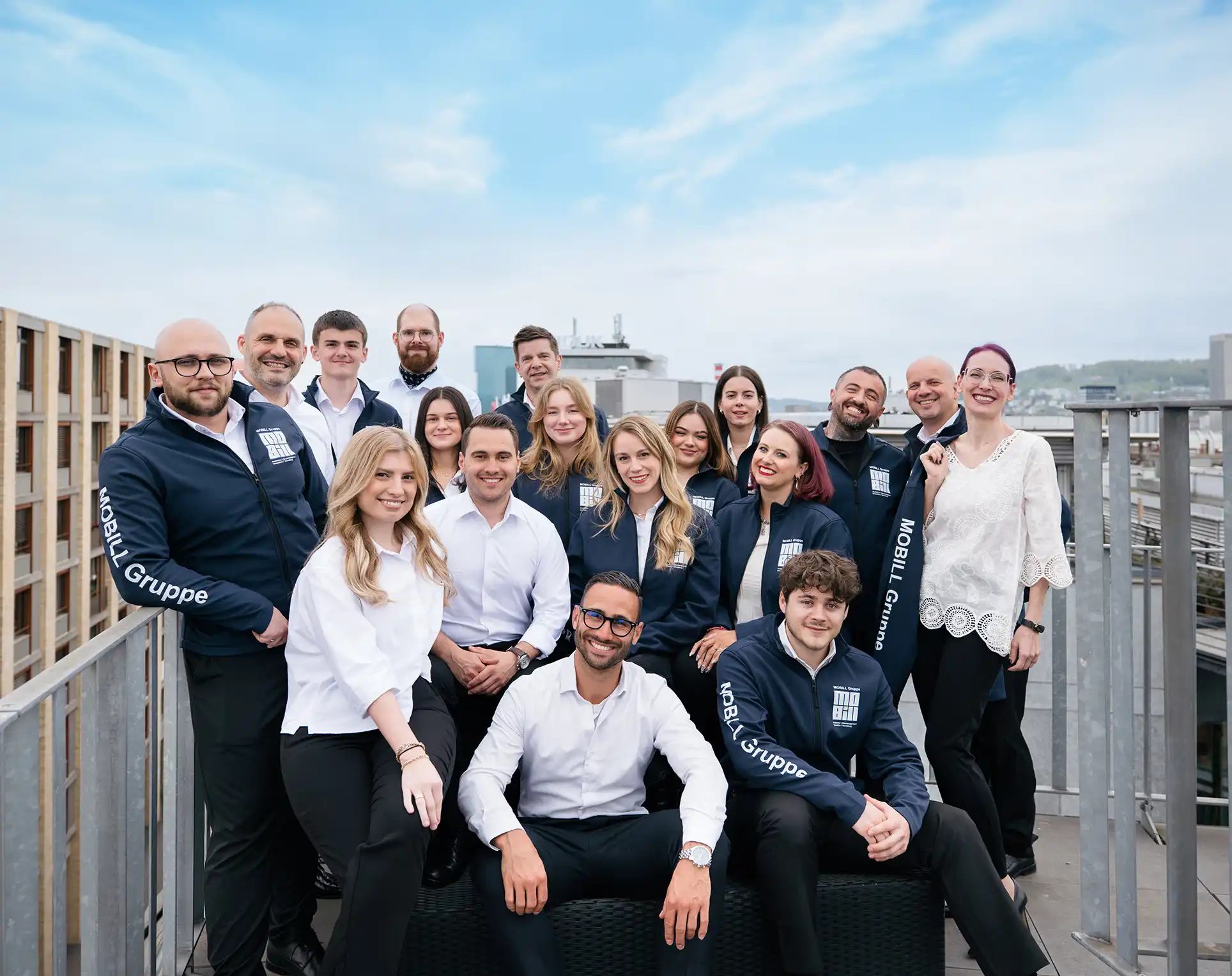 Gruppenfoto von 17 Personen auf einem Dach mit blauen Jacken der MOBILL Gruppe und weißer Bekleidung.
