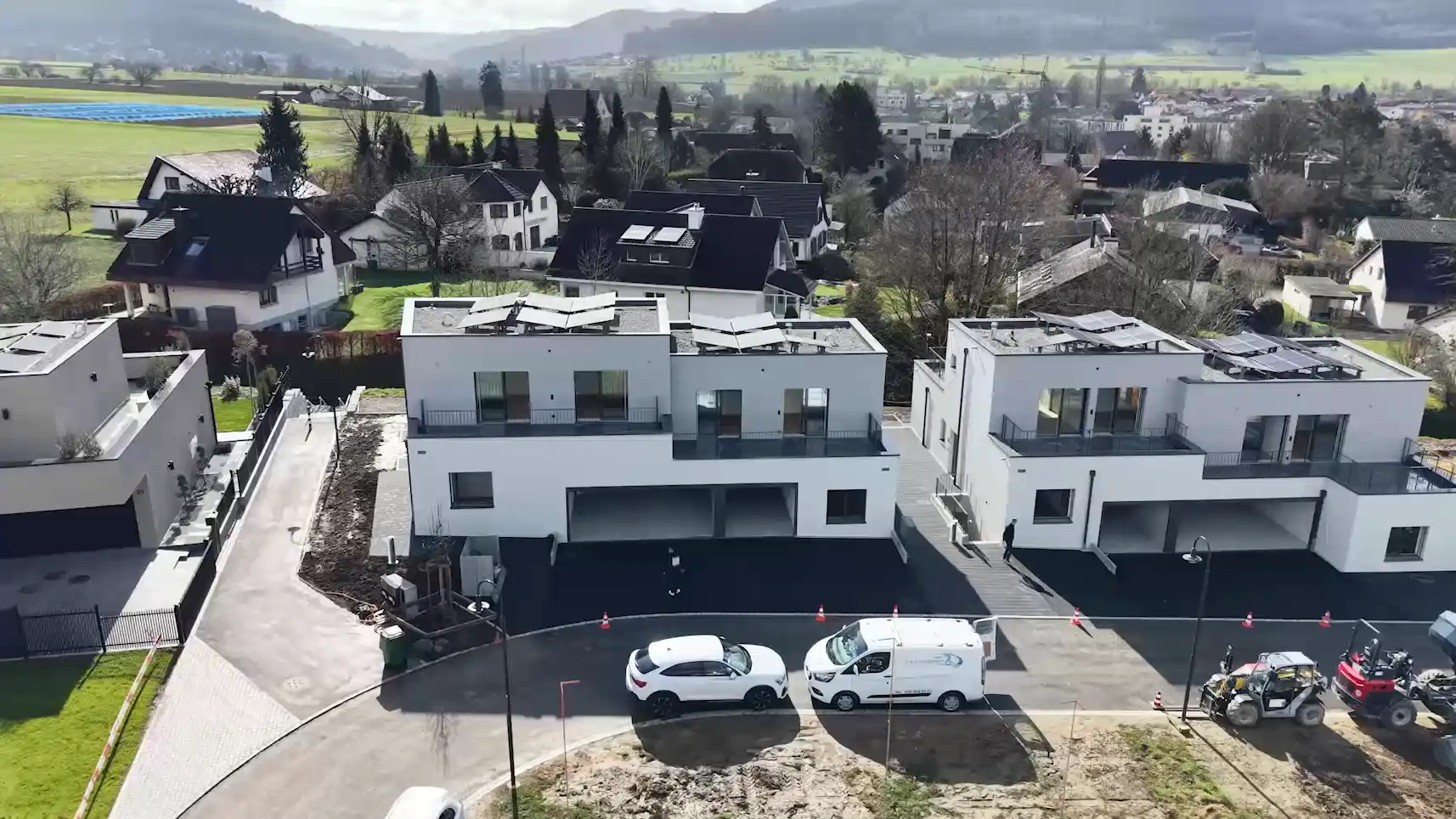 Moderne Wohnhäuser mit Solarplatten auf Dächern in einer ruhigen Vorstadt mit Bergen im Hintergrund.