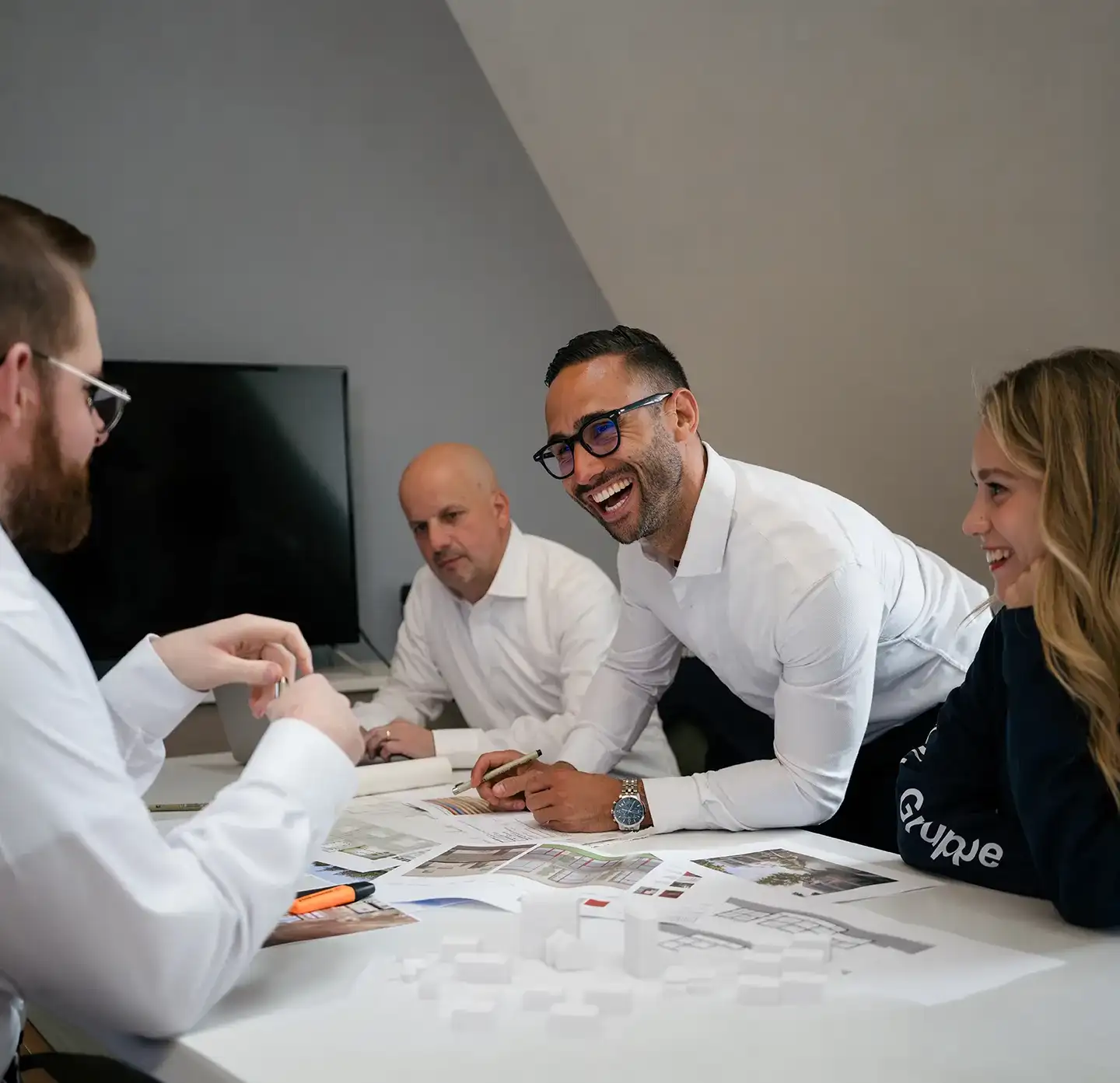 Vier Personen in einem Meeting diskutieren, lächeln und betrachten Pläne auf dem Tisch.
