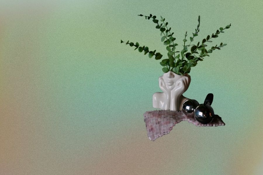 White ceramic vase shaped like a contemplative face with green leaves against a colorful gradient backdrop.