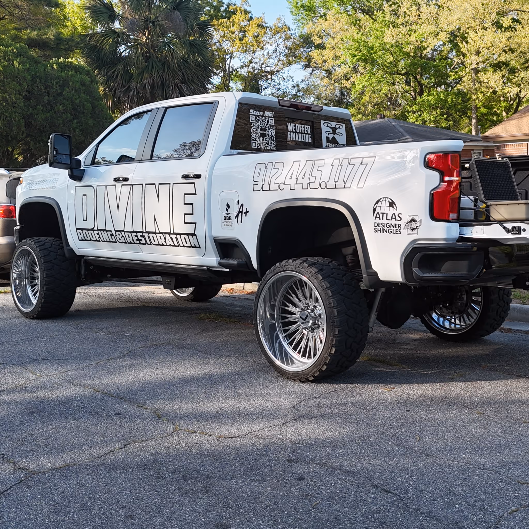 White pickup truck with large custom wheels displaying Divine Roofing & Restoration branding and contact number.
