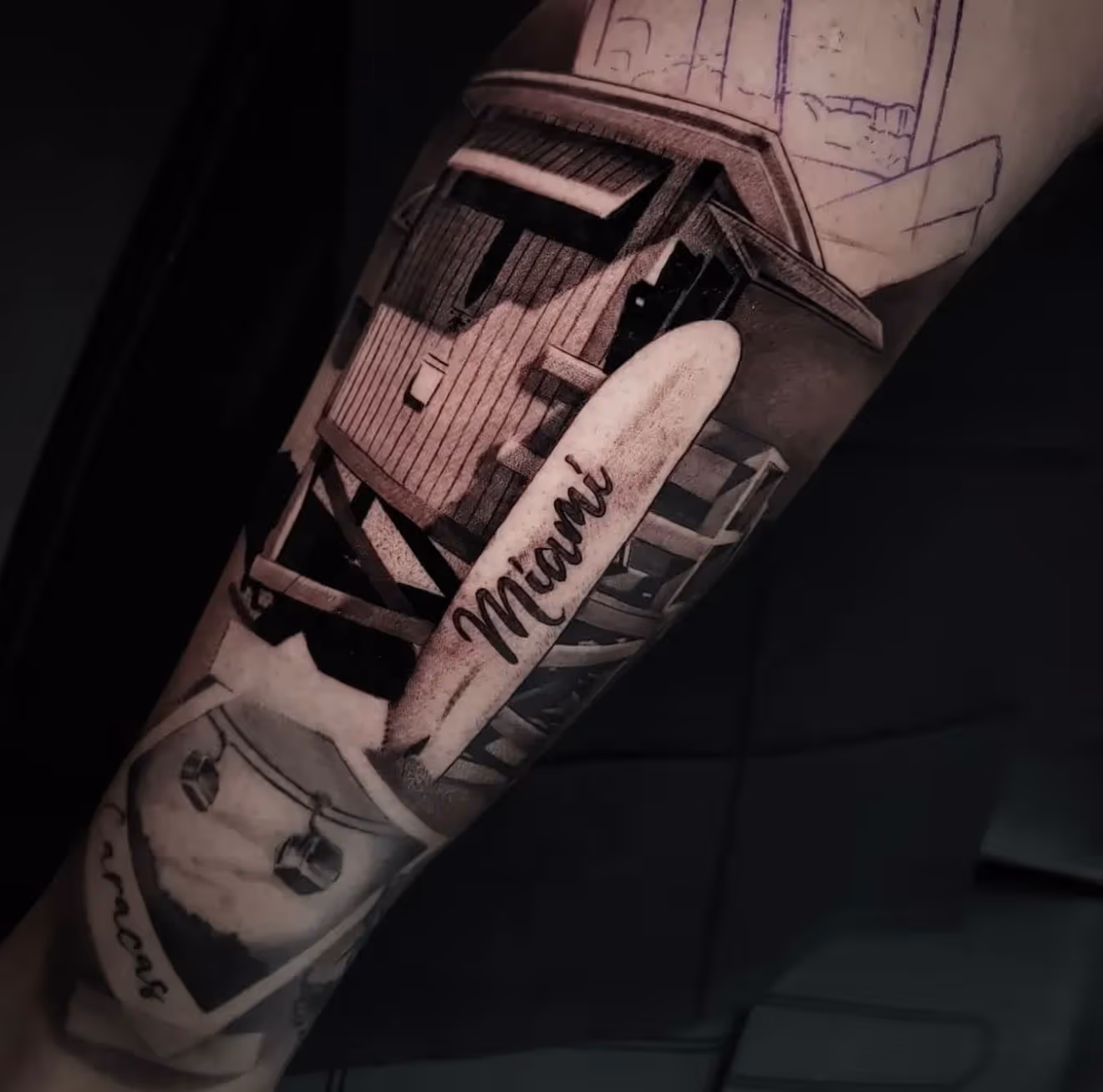 Black and gray tattoo of a lifeguard tower with a surfboard labeled 'Miami' on a person's arm.