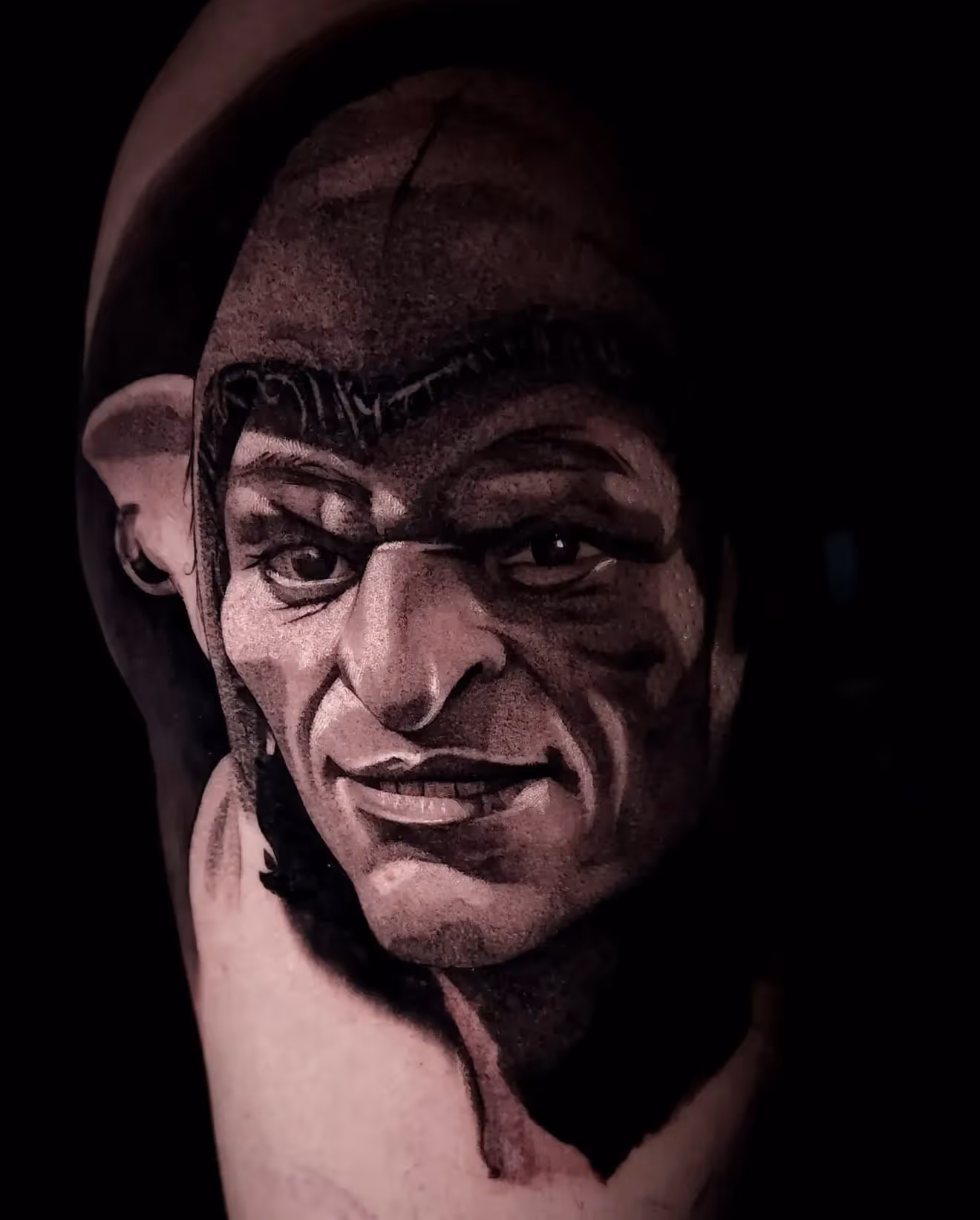 Black and gray tattoo portrait of a man's face with strong facial features and a prominent brow.
